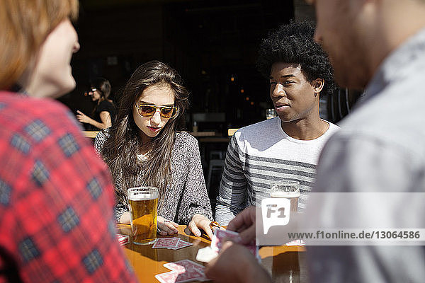 Friends playing cards while having beer at table in brewery