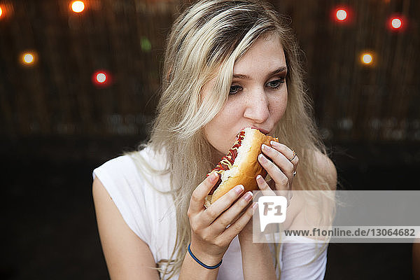 Frau mit blonden Haaren isst Hot Dog auf Gartenparty