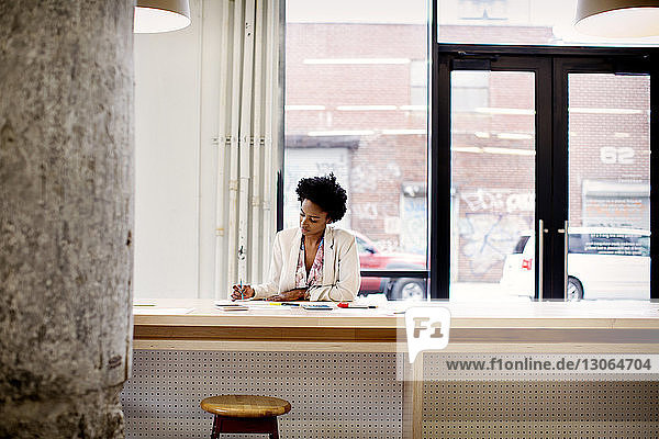 Seitenansicht einer Frau  die ein Buch liest  während sie im Büro an einem Regal steht