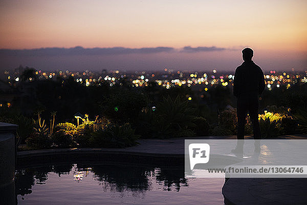 Silhouette man standing on poolside at dusk