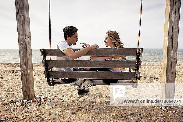Side view of couple sitting on swing at beach