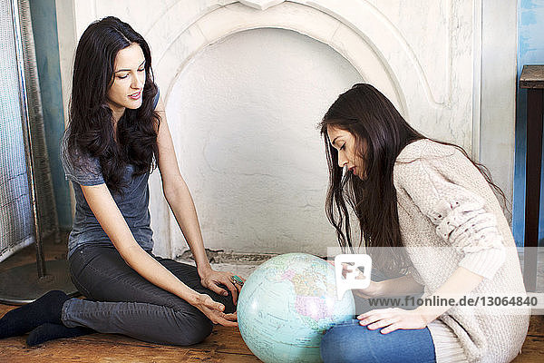 Sisters looking at globe while sitting on floor at home