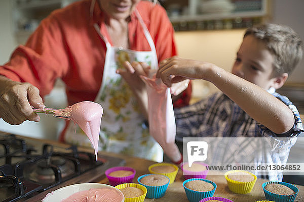 Woman with grandson filling cupcake holders in kitchen