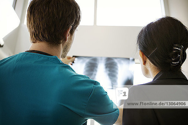 Rückansicht eines Arztes  der einer Geschäftsfrau im Krankenhaus ein Röntgenbild zeigt