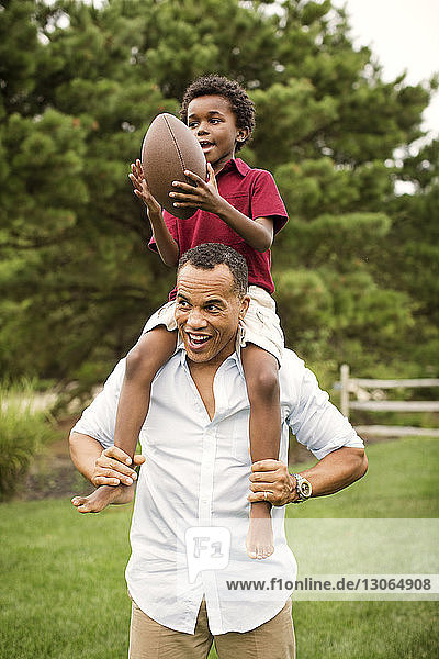 Man carrying son holding football ball while walking in backyard
