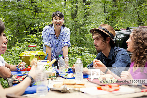 Woman looking friends having food at picnic table in forest