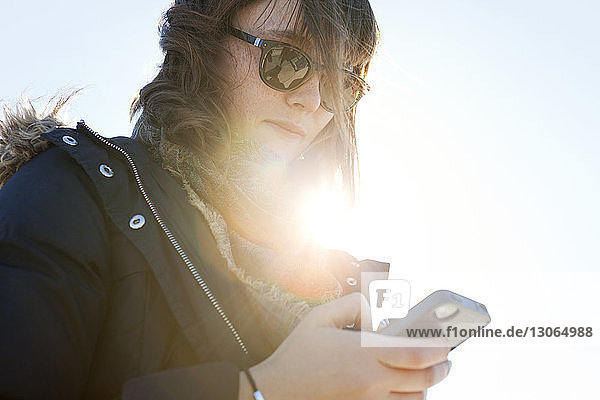 Niedrigwinkelansicht einer Frau  die an einem sonnigen Tag ein Smartphone benutzt