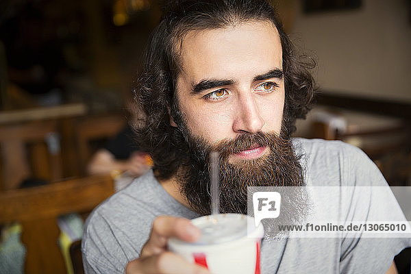Close-up of thoughtful man with beard drinking cola while sitting at cafe