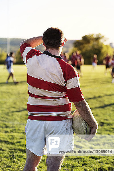 Rear view of rugby player holding ball while standing on grassy field