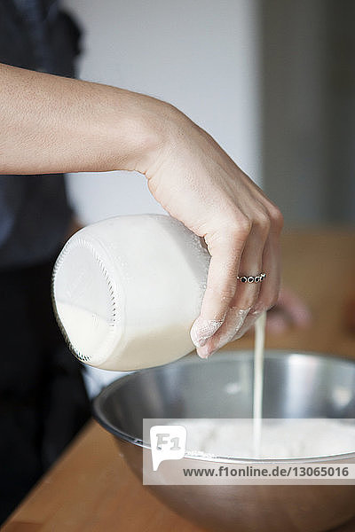 Beschnittenes Bild einer Hand  die Milch auf Mehl in einer Schüssel gießt