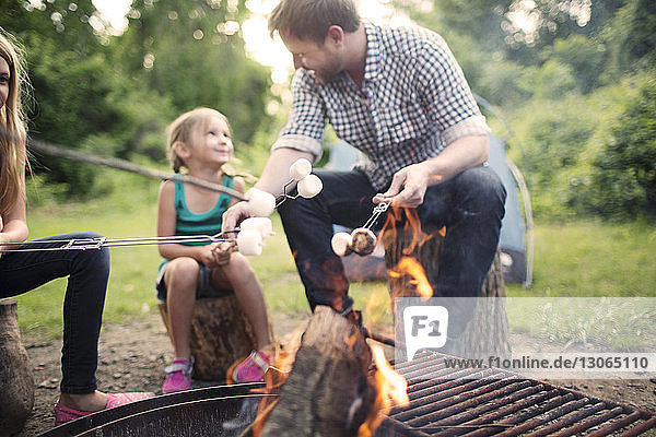 Father and daughter talking with roasting marshmallows at campfire