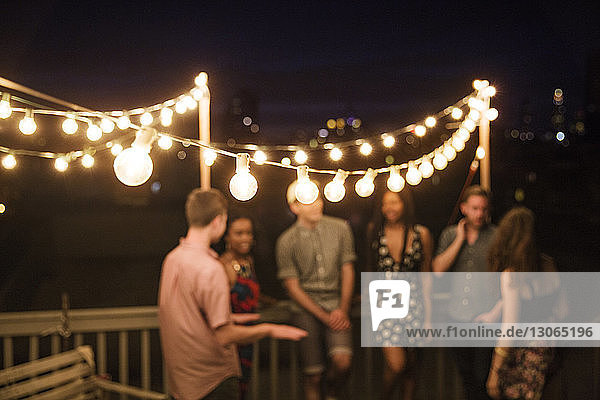 Freunde unterhalten sich  während sie nachts auf der Terrasse des Gebäudes am Geländer stehen