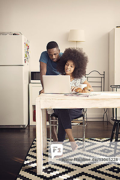 Couple using laptop computer at table with croissants in kitchen