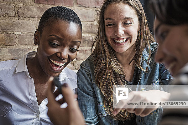 Frau zeigt Freunden ihr Smartphone  während sie im Café sitzt