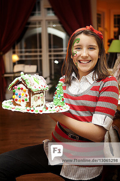 Porträt eines lächelnden Mädchens mit Gesichtsbemalung  das Lebkuchenhaus hält