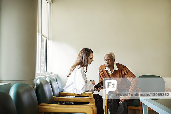 Arzt zeigt älteren Mann Bericht  während er im Krankenhaus auf Stühlen sitzt