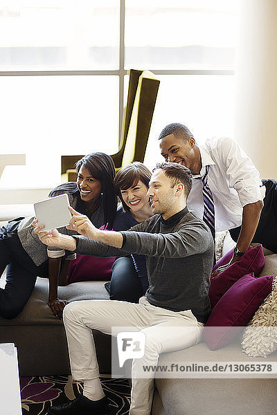 Cheerful colleagues taking selfie while sitting on sofa in office