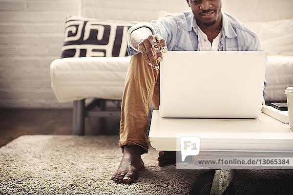 Smiling man using laptop computer while sitting on carpet at home