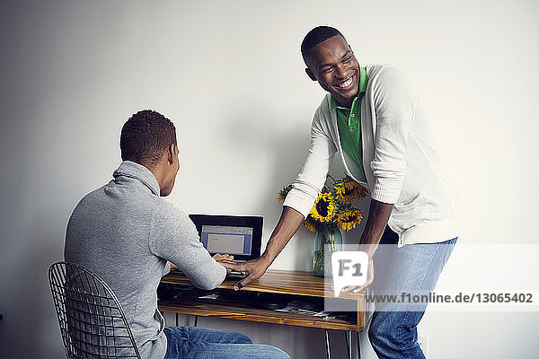 Schwuler Mann benutzt Laptop-Computer  während sein Freund am Tisch steht