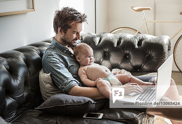 Glücklicher Mann benutzt Laptop-Computer  während er mit seinem Sohn zu Hause sitzt