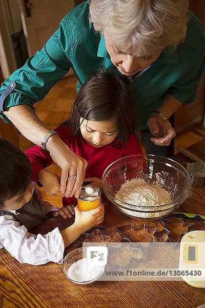 Schrägaufnahme einer Großmutter mit Kindern  die zu Hause Kekse backen