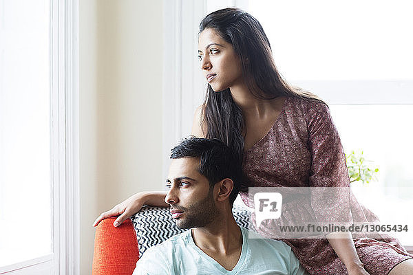 Nachdenkliches Paar schaut weg  während es sich zu Hause auf einem Sessel entspannt