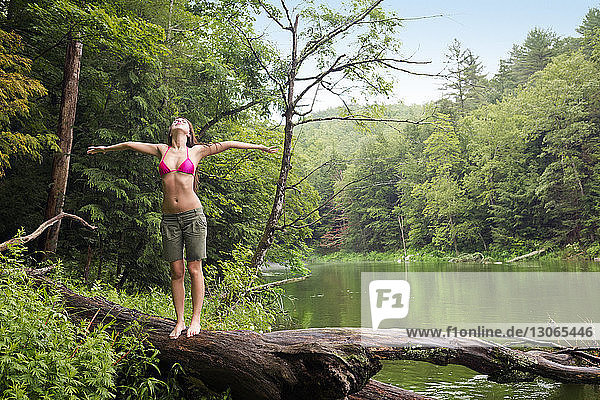 Woman with arms outstretched standing on fallen tree trunk at lakeshore
