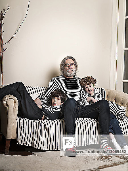 Portrait of grandfather sitting with grandsons on sofa at home