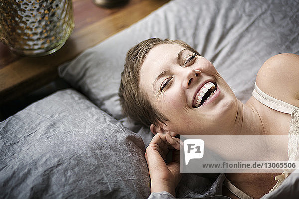 Hochwinkelansicht einer Frau  die lacht  während sie zu Hause auf dem Bett liegt