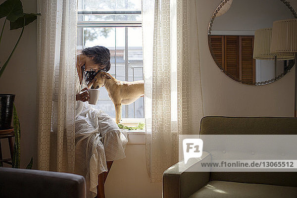 Woman with dog sitting on window sill at home