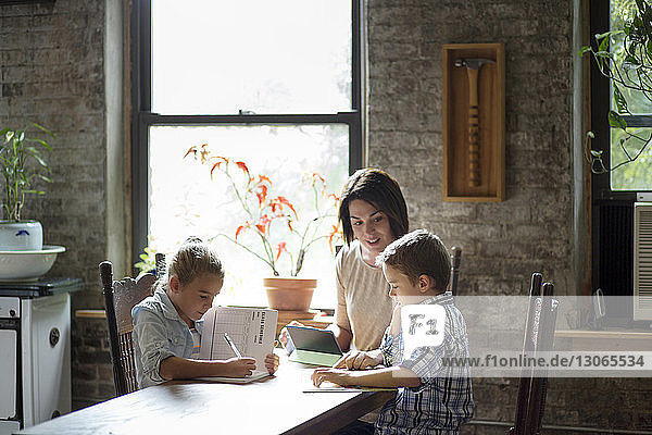 Mother assisting children in doing homework while sitting at table
