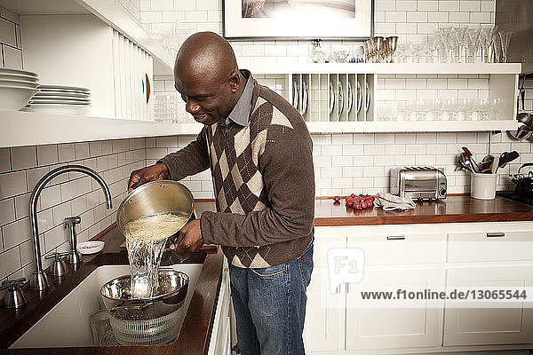 Mann wäscht zu Hause Spaghetti in Geschirr