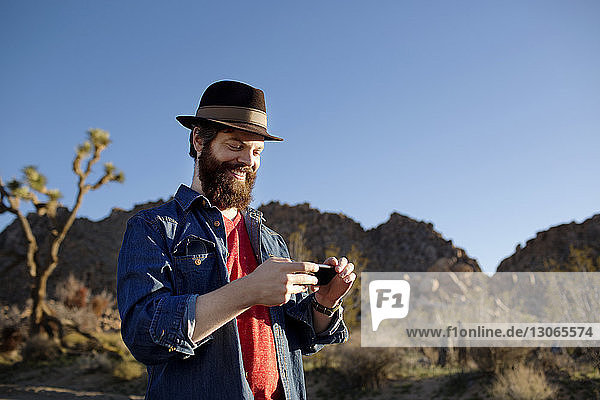 Niedrigwinkelansicht eines Mannes  der ein Mobiltelefon gegen klaren Himmel benutzt
