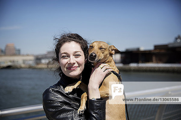 Portrait of happy woman with dog standing on footbridge against sky