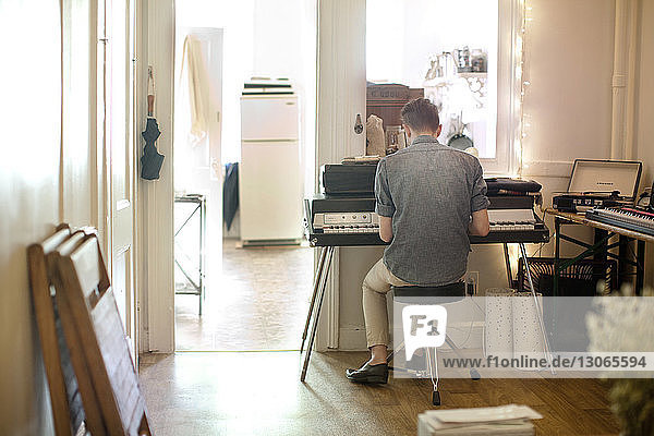 Rear view of man playing piano at home