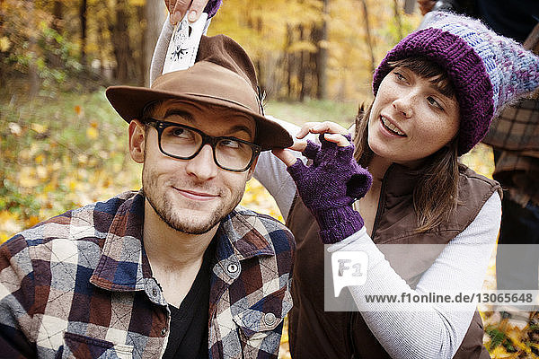 Playful woman putting card in man's hat at field