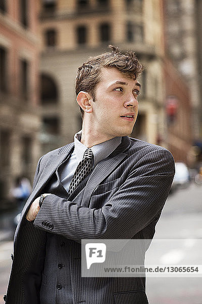 Businessman with hand in pocket looking away while standing on road in city