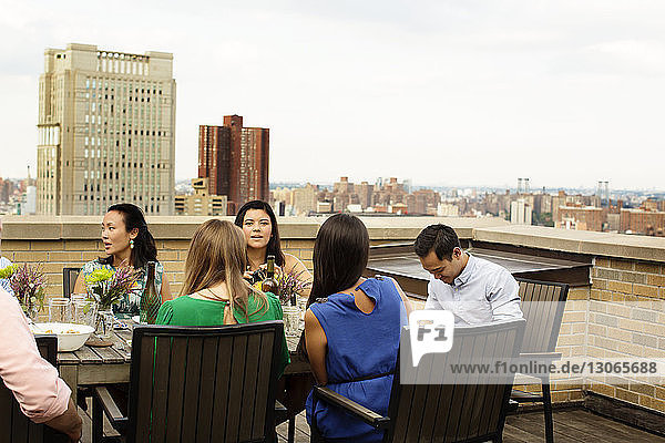 Friends having meal at table on building terrace against clear sky