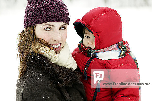 Porträt einer glücklichen Mutter  die mit ihrem Sohn auf einem schneebedeckten Feld steht