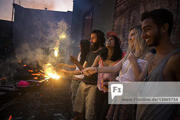Happy friends enjoying with lit sparklers at garden party during sunset