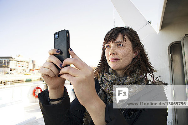 Woman photographing through mobile phone while traveling in passenger craft