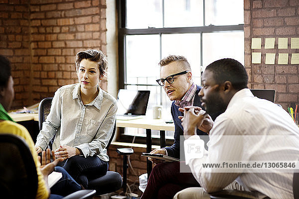 Business people listening to woman during meeting in office