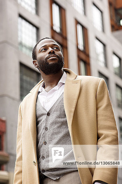 Low angle view of businessman looking away while standing against buildings