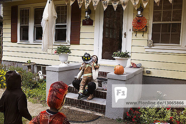 Frau umarmt einen Jungen im Halloween-Kostüm während eines Streichs oder einer Behandlung