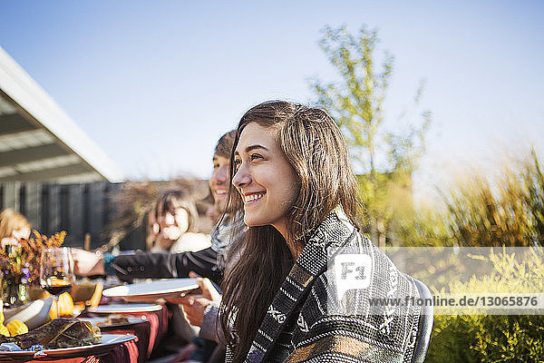 Seitenansicht einer glücklichen Frau  die während einer Gartenparty mit einem Freund an einem Tisch im Freien sitzt