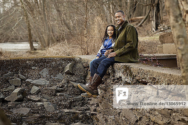 Portrait of father and daughter sitting on retaining wall