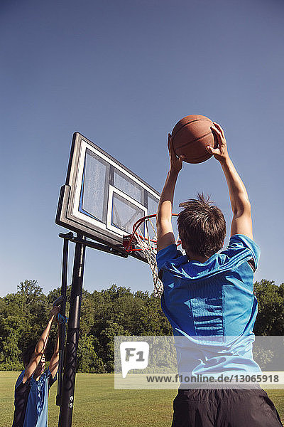Boys playing basketball by trees against clear sky