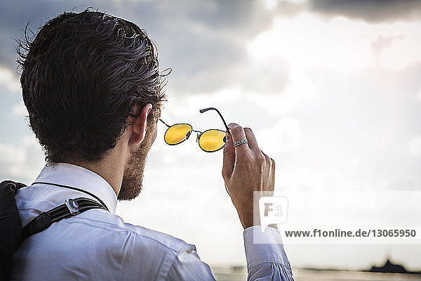 Rear view of businessman with sunglasses looking against sky