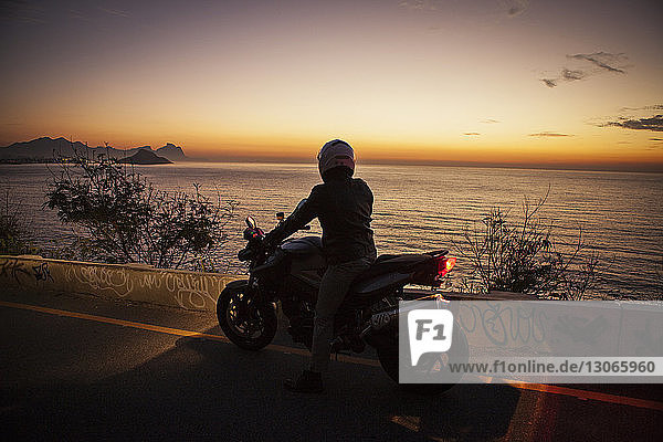 Rear view of man riding motorcycle by sea during sunset