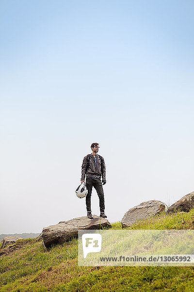 Man looking away while standing on rocks against clear sky